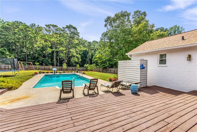 view of swimming pool with a deck, a trampoline, and a yard