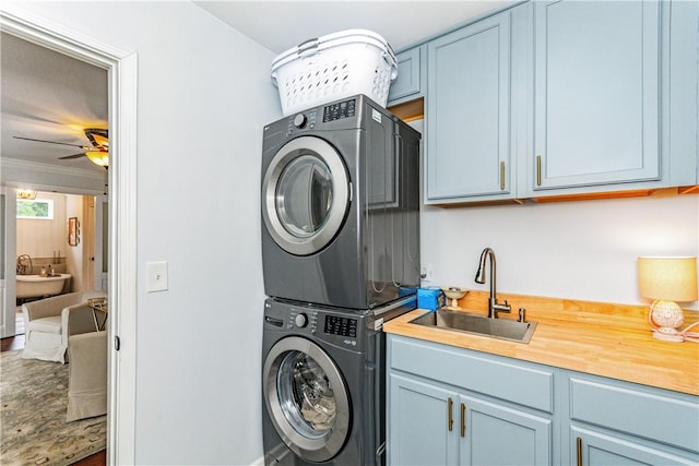 laundry area with cabinets, stacked washing maching and dryer, ceiling fan, crown molding, and sink