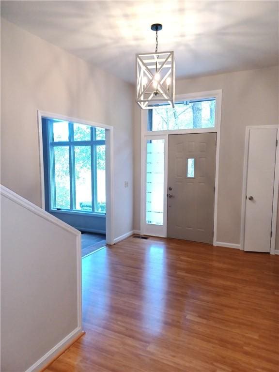 foyer entrance with a healthy amount of sunlight, an inviting chandelier, and hardwood / wood-style floors