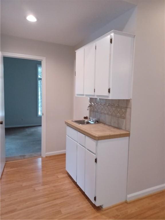 kitchen with decorative backsplash, sink, white cabinetry, and light hardwood / wood-style flooring