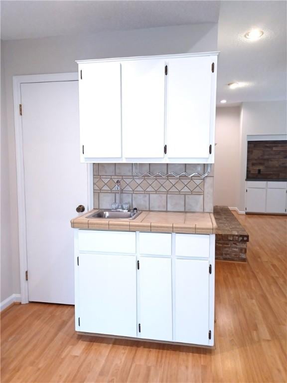 kitchen with tile counters, white cabinets, decorative backsplash, and light wood-type flooring