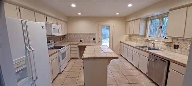 kitchen with white appliances, a kitchen island, white cabinetry, sink, and tile countertops