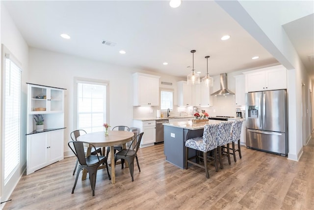 792 Village Dr, Opelika, AL 36801 - kitchen featuring stainless steel appliances, wall chimney exhaust hood, a kitchen island, white cabinetry, and a kitchen breakfast bar