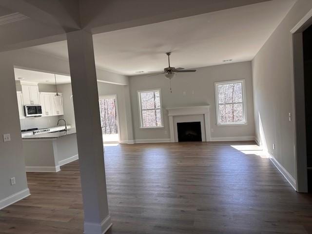 unfurnished living room featuring a ceiling fan, baseboards, a fireplace, a sink, and dark wood-type flooring