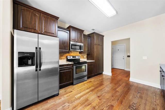 3204 Pinecrest Dr, Opelika, AL 36801 - kitchen with appliances with stainless steel finishes, dark brown cabinetry, backsplash, light wood-style flooring, and light stone counters