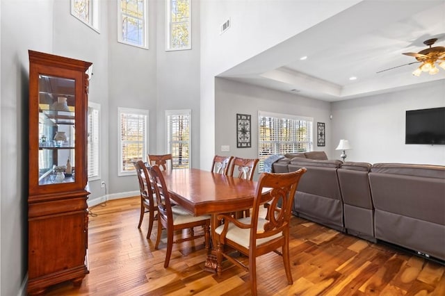 dining space featuring hardwood / wood-style floors, ceiling fan, a raised ceiling, and a high ceiling