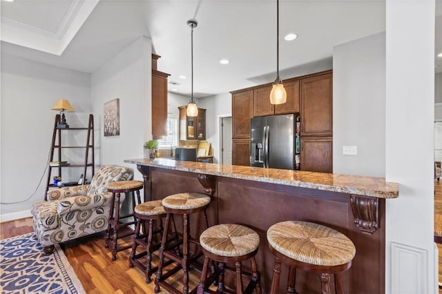 kitchen featuring a breakfast bar area, kitchen peninsula, pendant lighting, and stainless steel refrigerator with ice dispenser