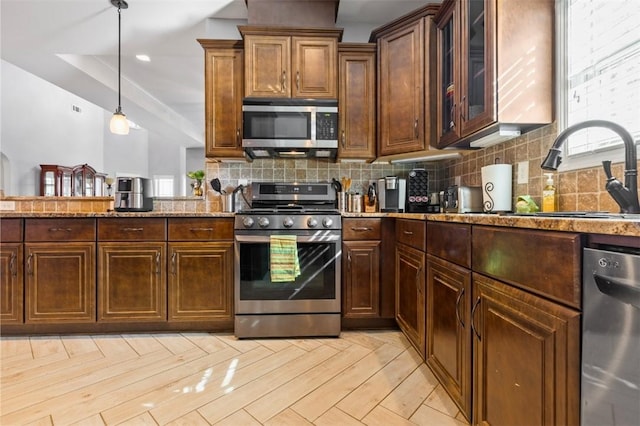 kitchen featuring sink, hanging light fixtures, stainless steel appliances, light stone counters, and decorative backsplash