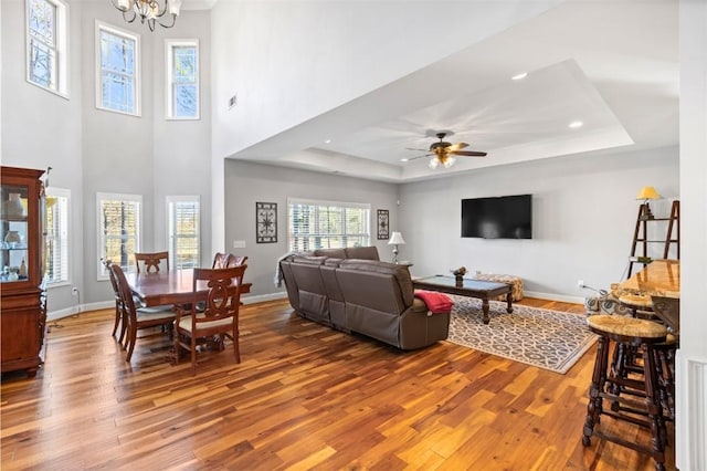 living room featuring a raised ceiling, hardwood / wood-style floors, and ceiling fan with notable chandelier