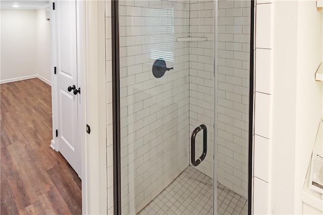bathroom with a stall shower, wood finished floors, and baseboards