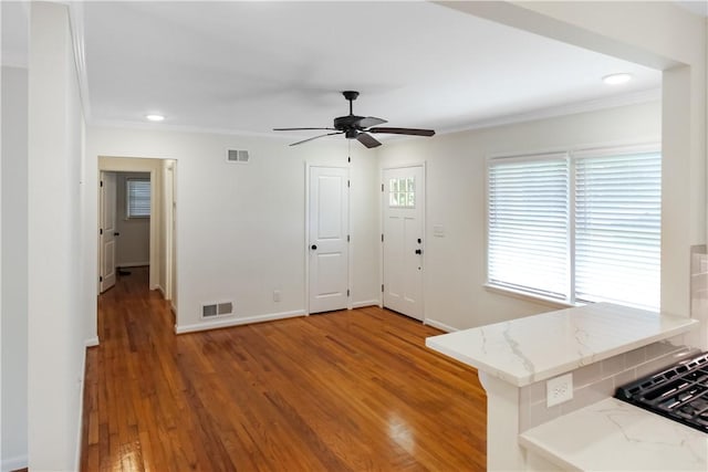 interior space with ornamental molding, visible vents, a ceiling fan, and wood finished floors
