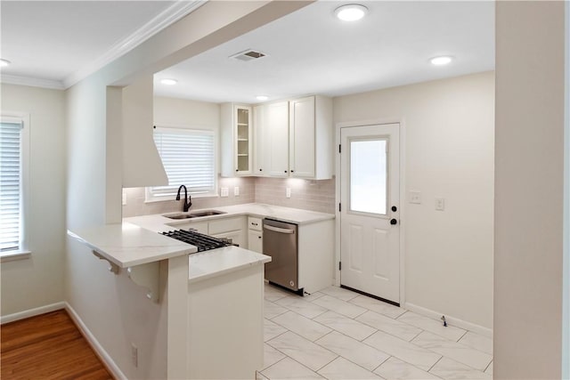 kitchen with visible vents, glass insert cabinets, a sink, a peninsula, and stainless steel dishwasher