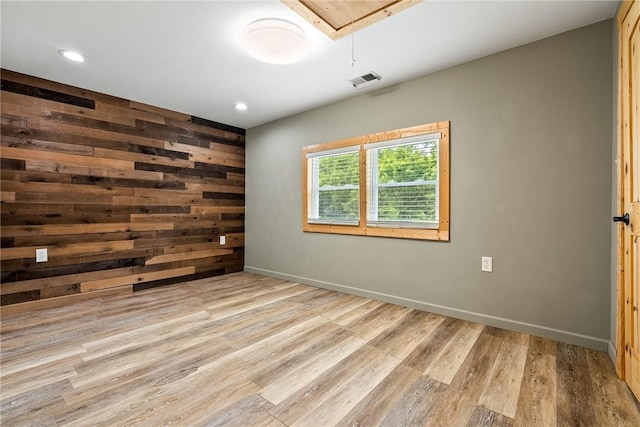 empty room featuring attic access, wood finished floors, baseboards, recessed lighting, and wooden walls