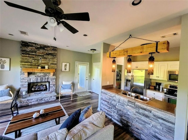 living room with a stone fireplace, ceiling fan, sink, and dark hardwood / wood-style floors