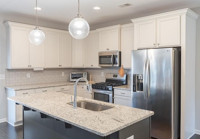 kitchen featuring sink, stainless steel appliances, light stone countertops, a center island with sink, and decorative light fixtures