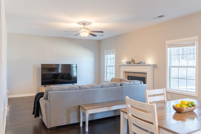 living room with ceiling fan, a healthy amount of sunlight, dark hardwood / wood-style floors, and a tile fireplace