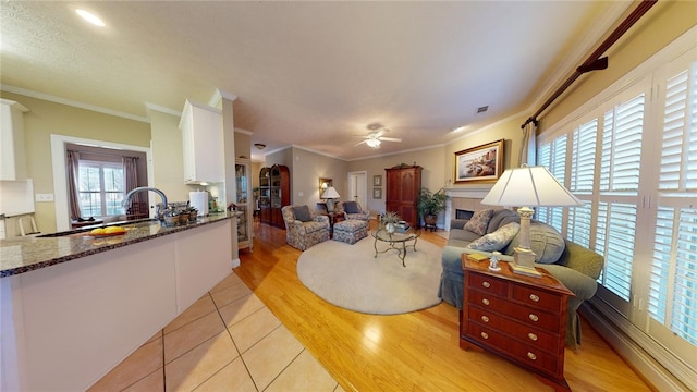 living room featuring ceiling fan, light tile patterned floors, a tile fireplace, and crown molding