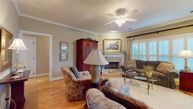 living room with a textured ceiling, light hardwood / wood-style flooring, ceiling fan, a tile fireplace, and crown molding