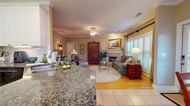 kitchen featuring white cabinetry, sink, ornamental molding, light tile patterned floors, and a tiled fireplace