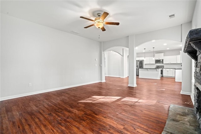 unfurnished living room featuring visible vents, wood finished floors, arched walkways, a stone fireplace, and ceiling fan