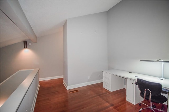 unfurnished office with dark wood-type flooring, built in desk, baseboards, and beam ceiling