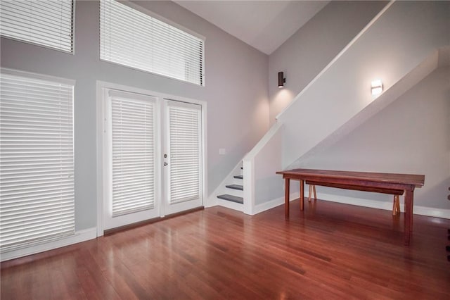 unfurnished living room with stairway, a high ceiling, wood finished floors, and baseboards