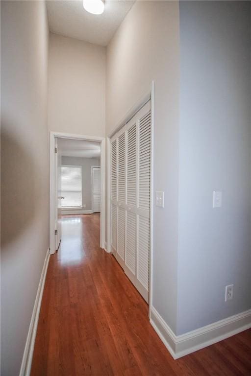 corridor with wood finished floors, baseboards, and a high ceiling