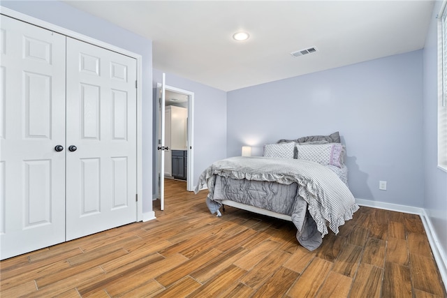 bedroom with a closet, visible vents, baseboards, and wood finished floors