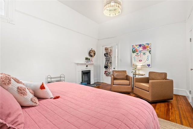 bedroom featuring a fireplace with flush hearth, wood finished floors, and baseboards