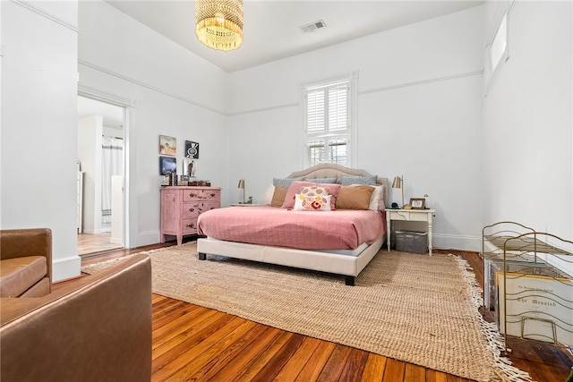 bedroom featuring ensuite bathroom, wood finished floors, visible vents, and baseboards