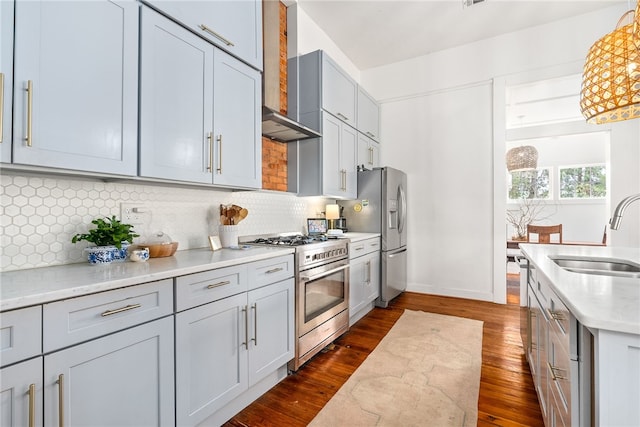 kitchen featuring tasteful backsplash, dark wood-type flooring, stainless steel appliances, wall chimney range hood, and a sink