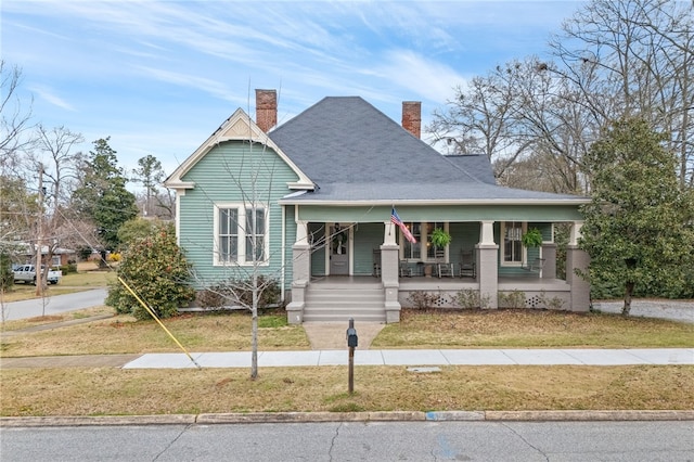 view of front facade with covered porch, a chimney, and a front lawn