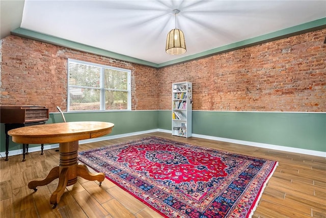 living area featuring brick wall, baseboards, and wood finished floors