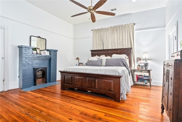 bedroom featuring baseboards, visible vents, a ceiling fan, hardwood / wood-style floors, and a fireplace