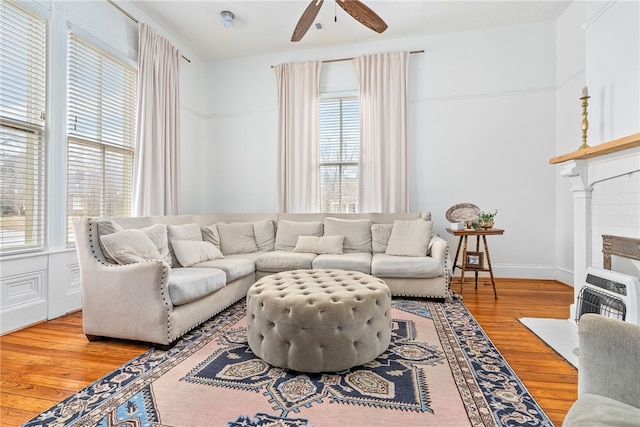 living area featuring baseboards, a fireplace with flush hearth, ceiling fan, wood finished floors, and heating unit