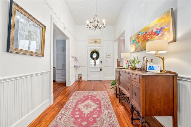 foyer with a wainscoted wall, light wood-type flooring, and an inviting chandelier