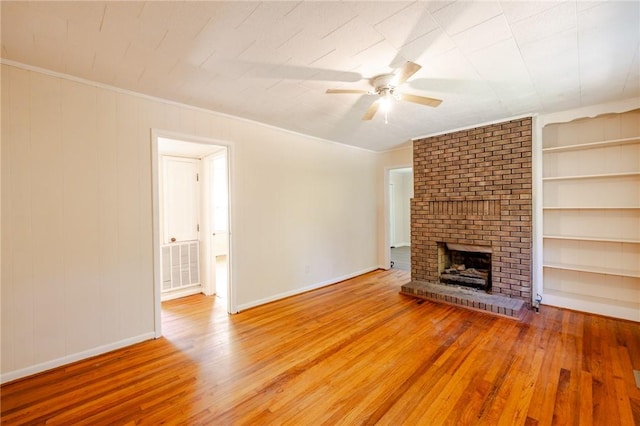 unfurnished living room featuring hardwood / wood-style floors, crown molding, ceiling fan, a brick fireplace, and built in features