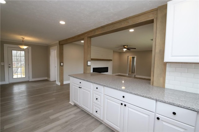 kitchen featuring white cabinetry, backsplash, light stone countertops, light hardwood / wood-style floors, and decorative light fixtures