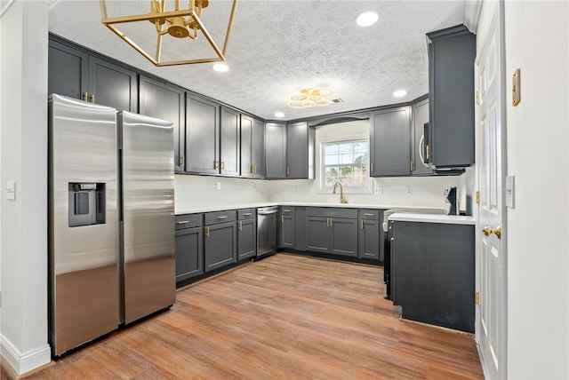 kitchen featuring light wood-type flooring, a textured ceiling, stainless steel appliances, and a sink