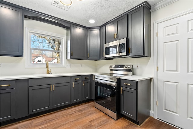 kitchen featuring stainless steel appliances, a sink, visible vents, light countertops, and light wood finished floors