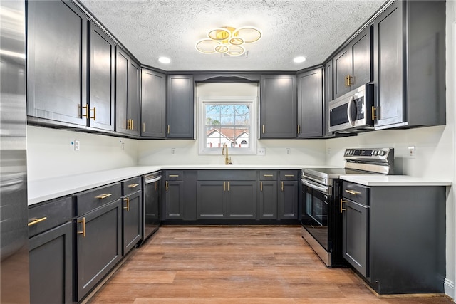 kitchen featuring a textured ceiling, stainless steel appliances, light wood-type flooring, and a sink