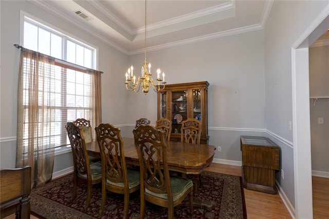 dining area featuring a tray ceiling, light wood-style floors, visible vents, and a wealth of natural light