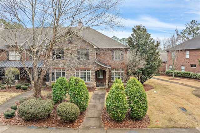 view of front of property featuring brick siding, stone siding, a chimney, and a shingled roof