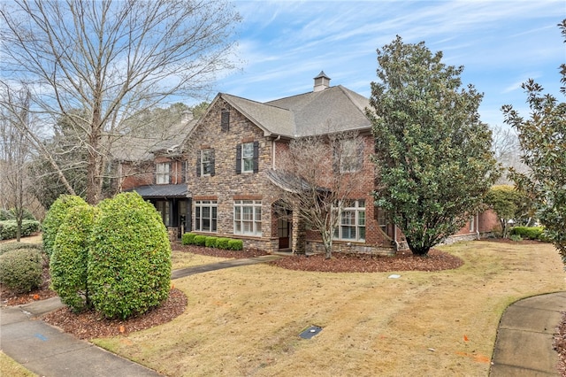 traditional-style house featuring stone siding, a front yard, and a chimney