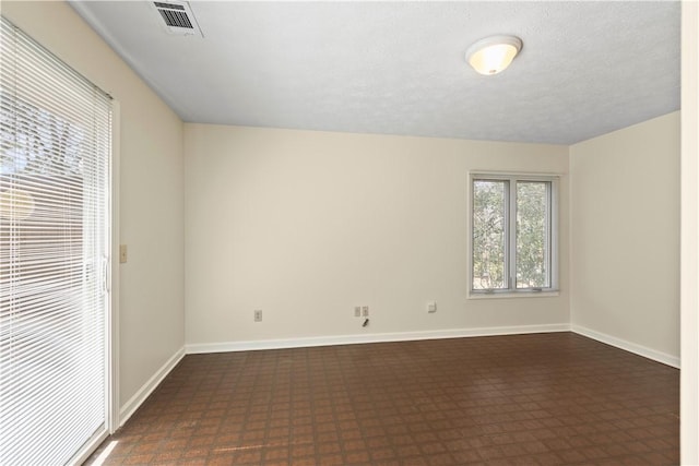 spare room featuring dark floors, visible vents, and baseboards