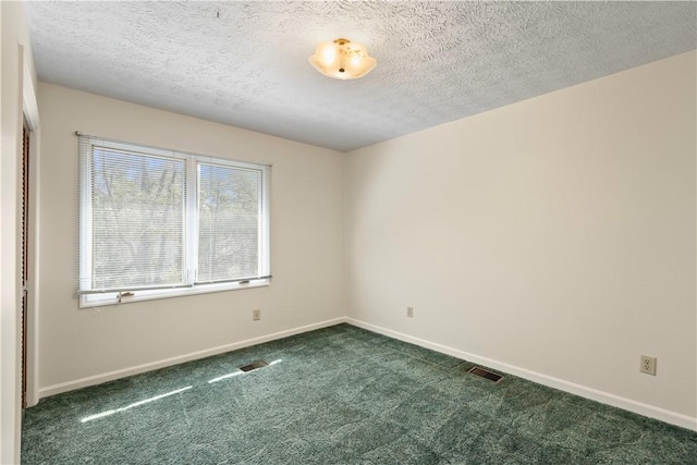 spare room featuring baseboards, visible vents, dark carpet, and a textured ceiling