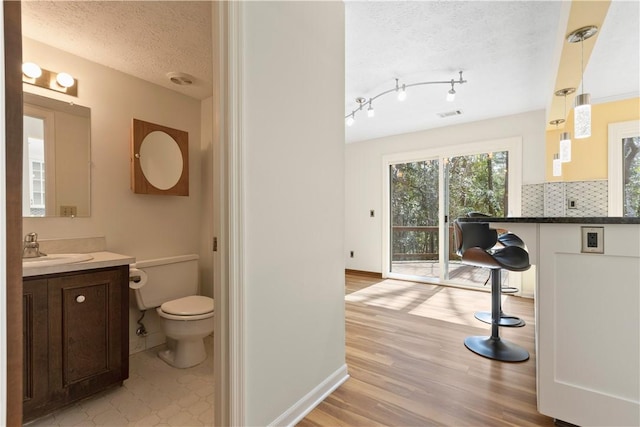 bathroom featuring decorative backsplash, toilet, wood finished floors, a textured ceiling, and vanity