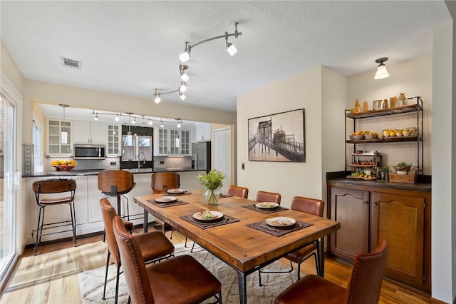 dining area featuring a textured ceiling, a healthy amount of sunlight, visible vents, and light wood-style floors