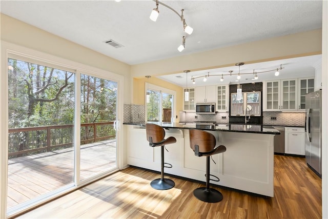 kitchen with wood finished floors, visible vents, appliances with stainless steel finishes, dark countertops, and glass insert cabinets