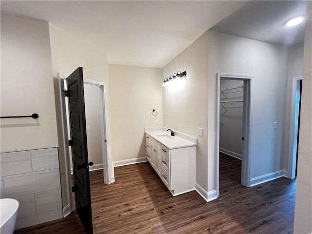 bathroom featuring vanity, baseboards, wood finished floors, and a spacious closet